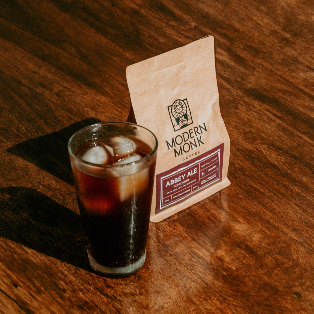 Glass of iced coffee with a 'Modern Monk' coffee package on a wooden surface