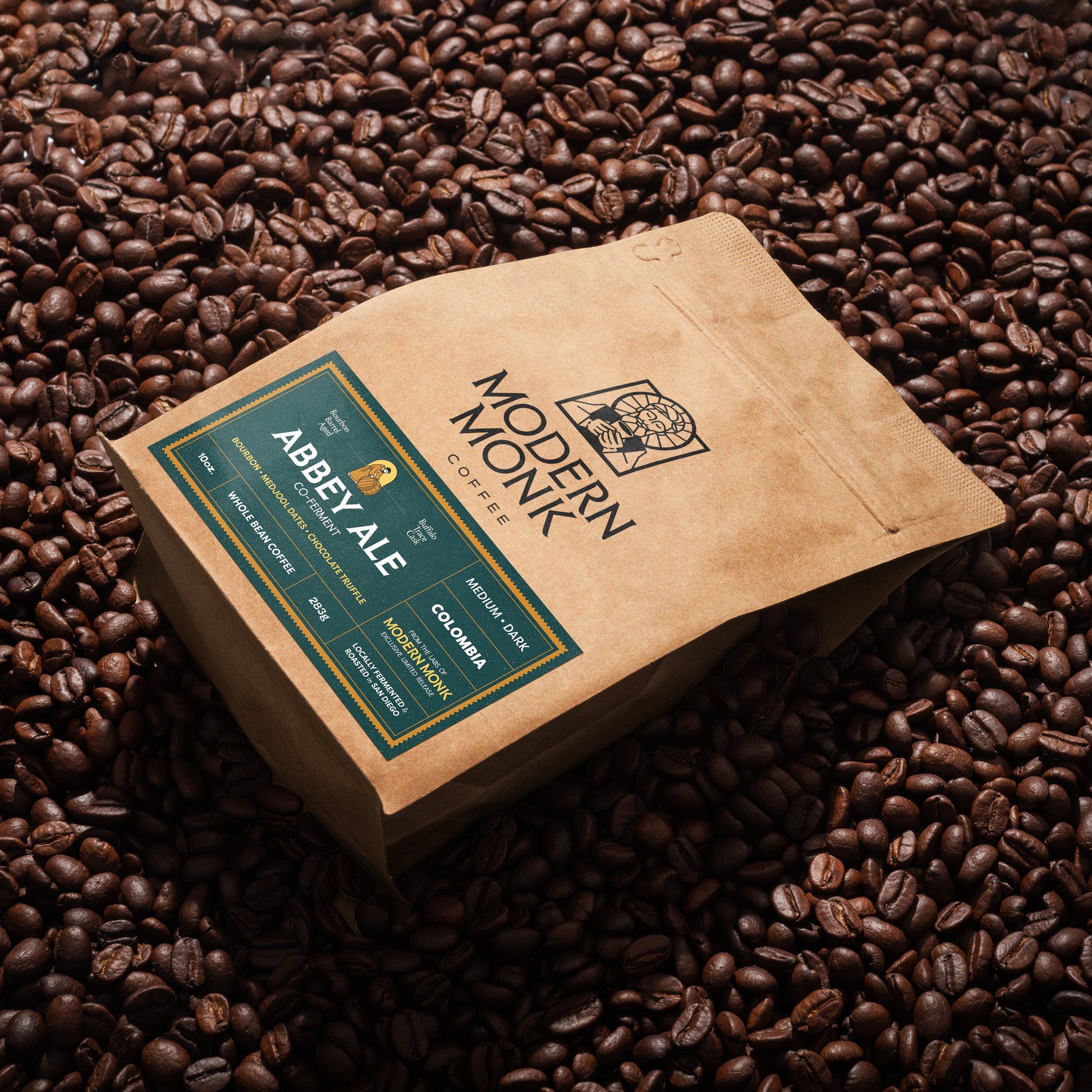 A kraft paper coffee bag labeled 'Modern Monk' and 'Abbete Ale' lies on top of a dense bed of roasted coffee beans.