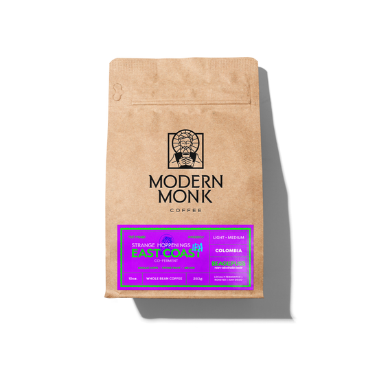 A brown paper coffee bag from Modern Monk Coffee, featuring a bright purple and green label at the bottom. The bag is photographed on a clean white background with a soft shadow cast to the right.